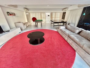 Un salon moderne avec un tapis rouge, une table basse ronde noire, un canapé beige, une table à manger et un téléviseur.