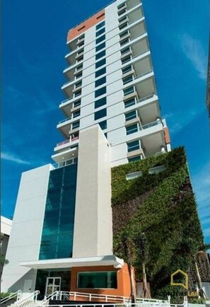 Un moderno edificio de gran altura con múltiples balcones, fachada de vidrio y jardín vertical cubierto de vegetación.