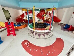 Un espace de jeux pour enfants avec un toboggan, un filet d’escalade et une piscine à balles.