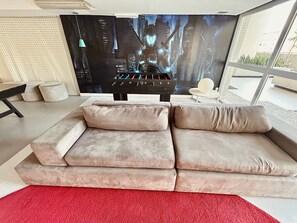Ein modernes Wohnzimmer mit einem großen Flachbildfernseher, einer Couch, einem roten Teppich und einem Kicker.