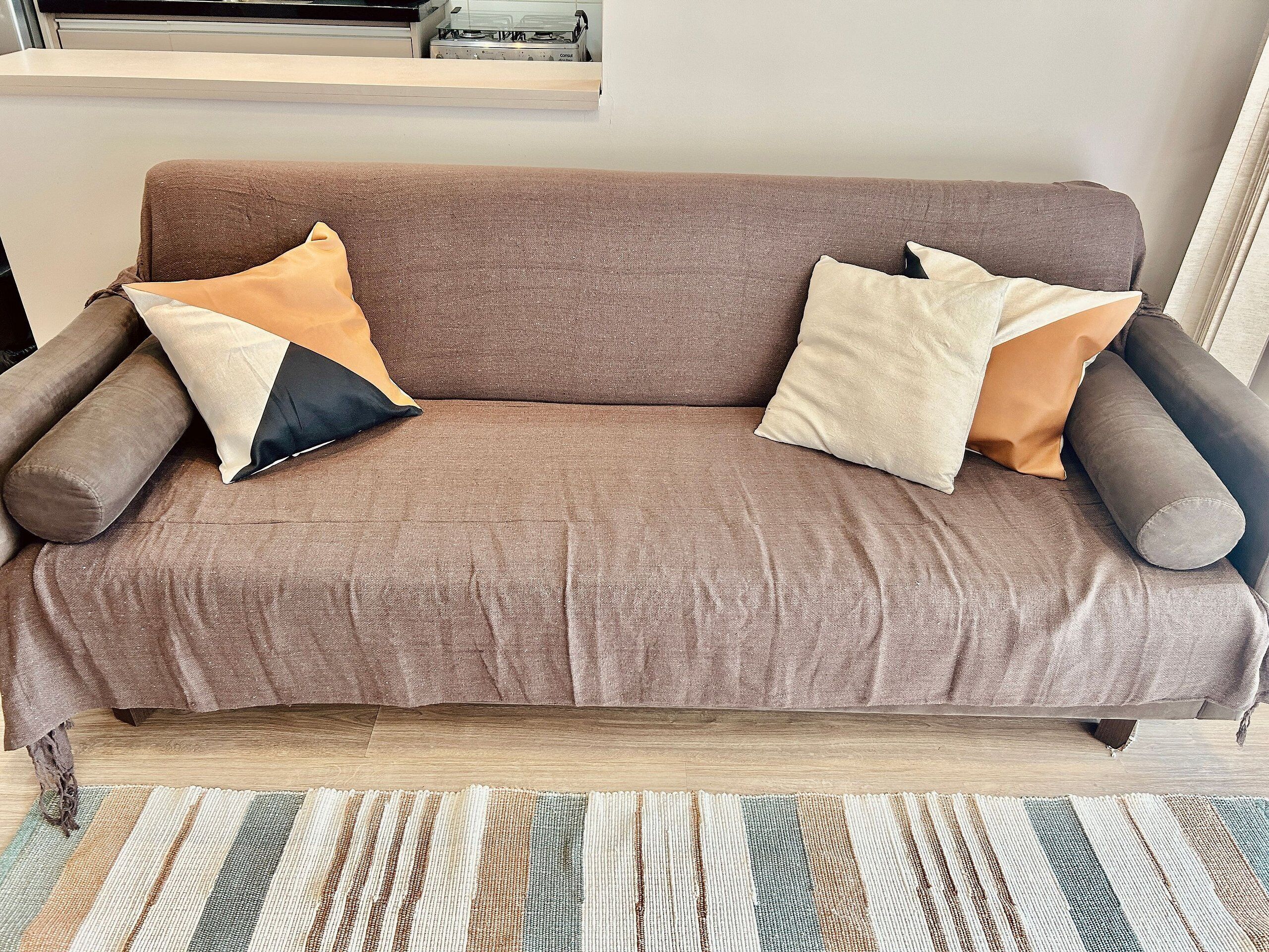 Un sofá marrón con varios cojines en una habitación con suelo de madera y un alfombra a rayas.