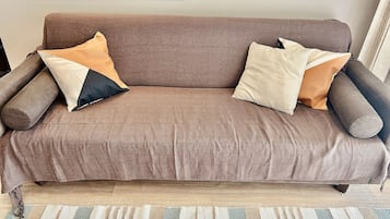 Un sofá marrón con varios cojines en una habitación con suelo de madera y un alfombra a rayas.