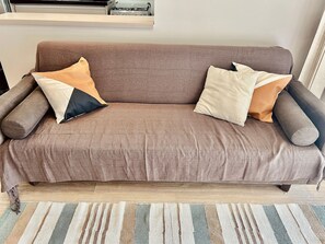 Un canapé marron agrémenté de plusieurs coussins, dans une pièce dotée d’un plancher en bois et d’un tapis à rayures.