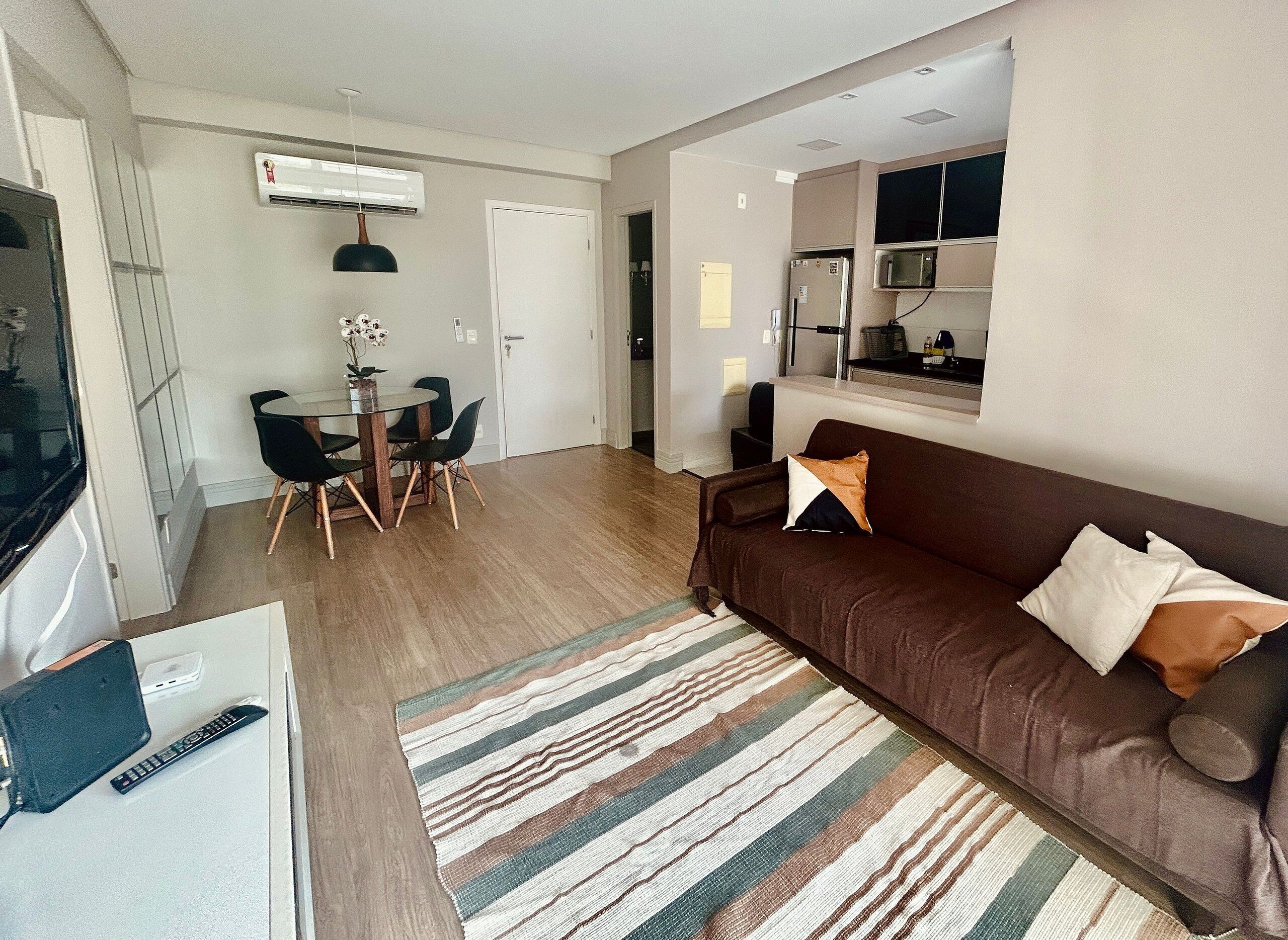 A living room with a brown sofa, a striped rug, a dining table with chairs, and a TV.