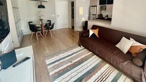 Ett vardagsrum med en brun soffa, en randig matta, ett matbord med stolar och en tv.