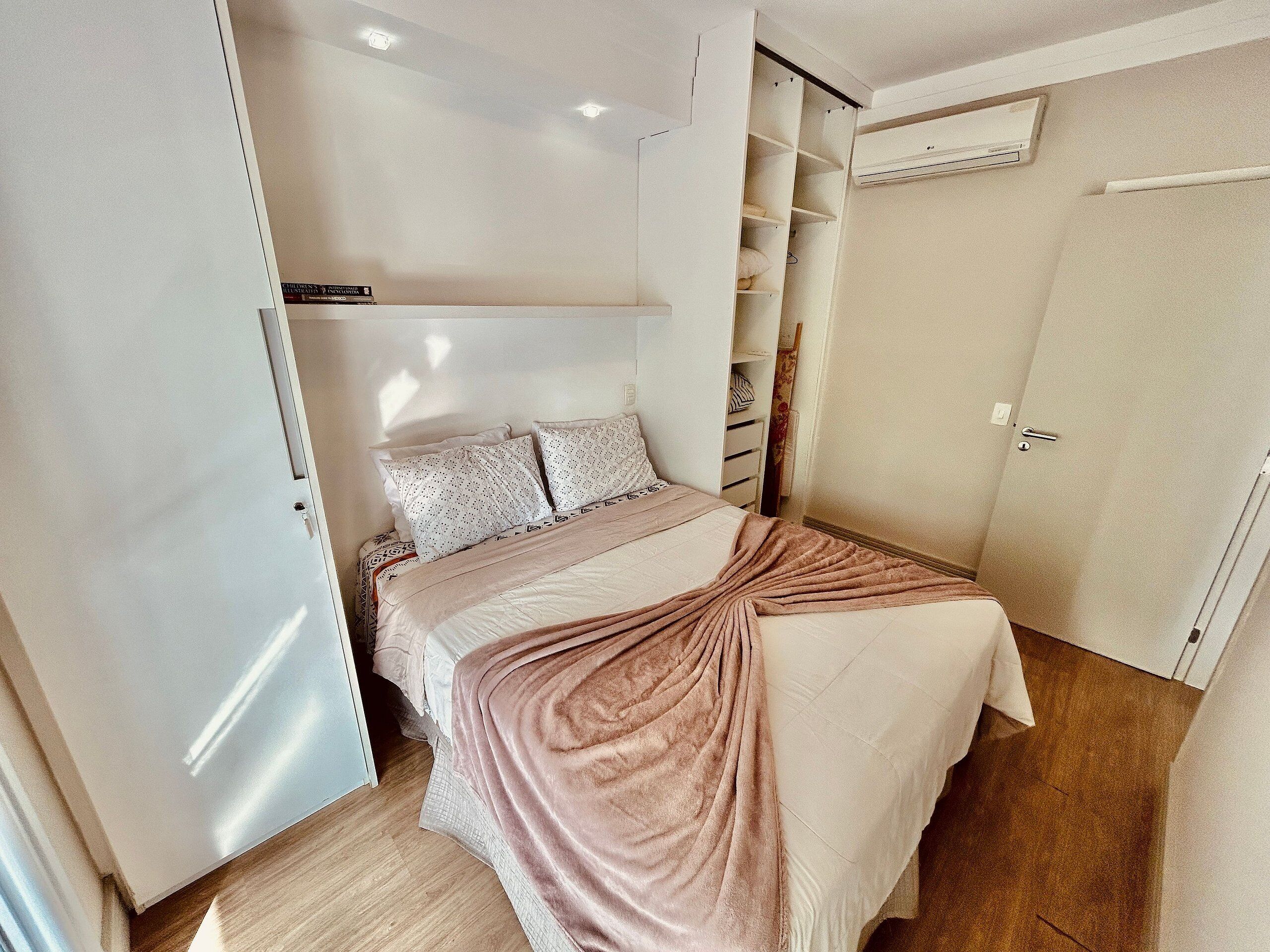 A bedroom with a bed, a wardrobe, and an air conditioning unit.