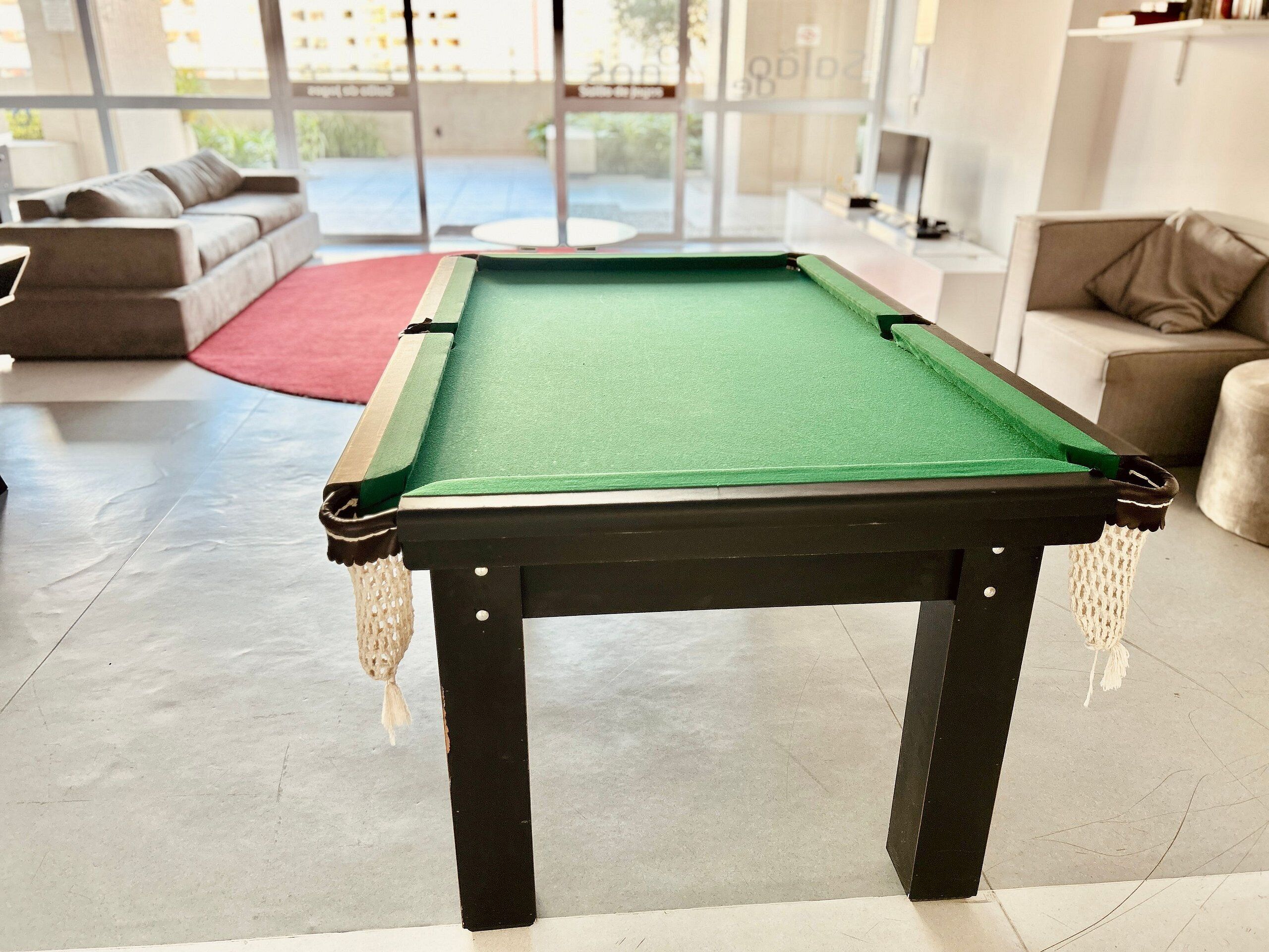Una mesa de billar en una sala de estar moderna con un sofá y una alfombra roja.