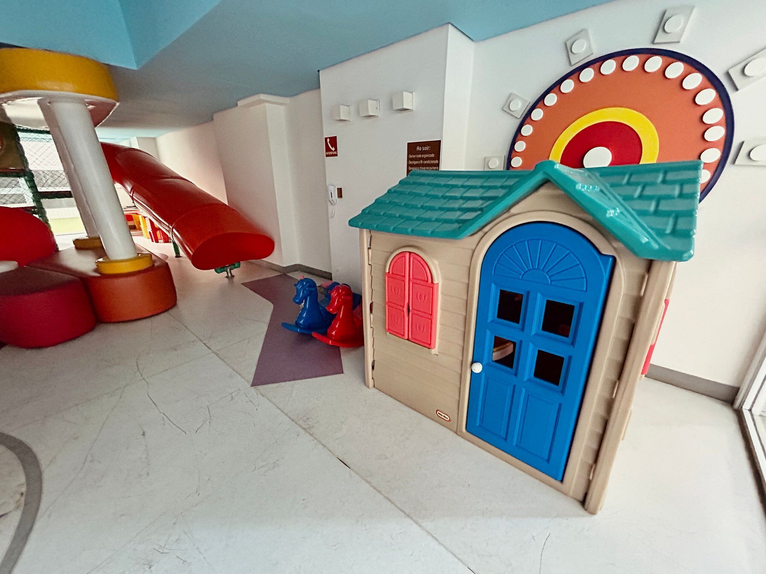 Een kinderspeelplaats met een glijbaan, een speelhuisje en kleurrijke wanddecoratie.