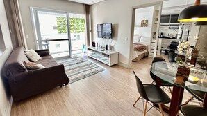 Ett modernt vardagsrum med en soffa, TV, matplats och utsikt genom en glasdörr.
