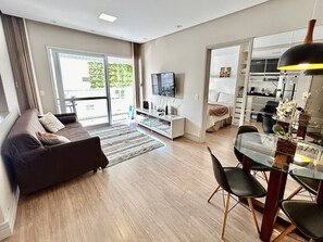 Un salon moderne comprenant un canapé, un téléviseur, un coin repas et une vue sur l’extérieur grâce à une porte vitrée.