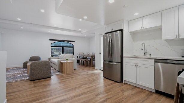 A modern kitchen with white cabinets, stainless steel appliances, and a dining area with a large window. - Lovely Beachside 2-Bedroom Apartment (Santa Monica)