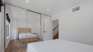 A modern bedroom with a glass partition, a wooden bed, and a staircase. - Lovely Beachside 2-Bedroom Apartment (Santa Monica)
