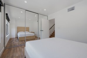 A modern bedroom with a glass partition, a wooden bed, and a staircase. - Lovely Beachside 2-Bedroom Apartment (Santa Monica)