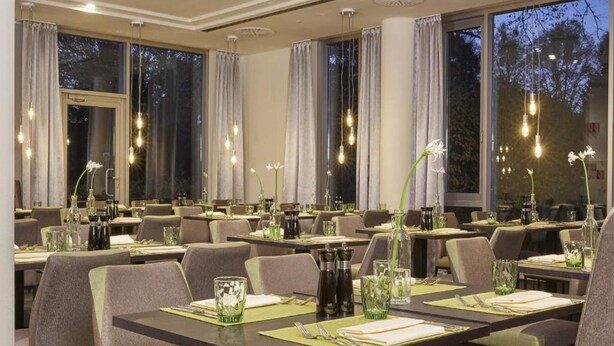 A restaurant with tables set for dining, large windows, and hanging light fixtures. - 4 Person Holiday Park Home in Kassel (Kassel)