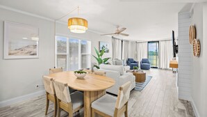 A modern living room with a dining area, large windows, and a ceiling fan. - Hutchinson Island Oceanfront Condo (Jensen Beach)