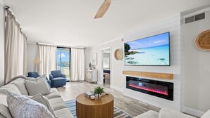 A modern living room with a sofa, a coffee table, a TV, and a fireplace. - Hutchinson Island Oceanfront Condo (Jensen Beach)
