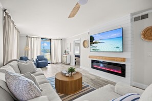 A modern living room with a sofa, a coffee table, a TV, and a fireplace. - Hutchinson Island Oceanfront Condo (Jensen Beach)