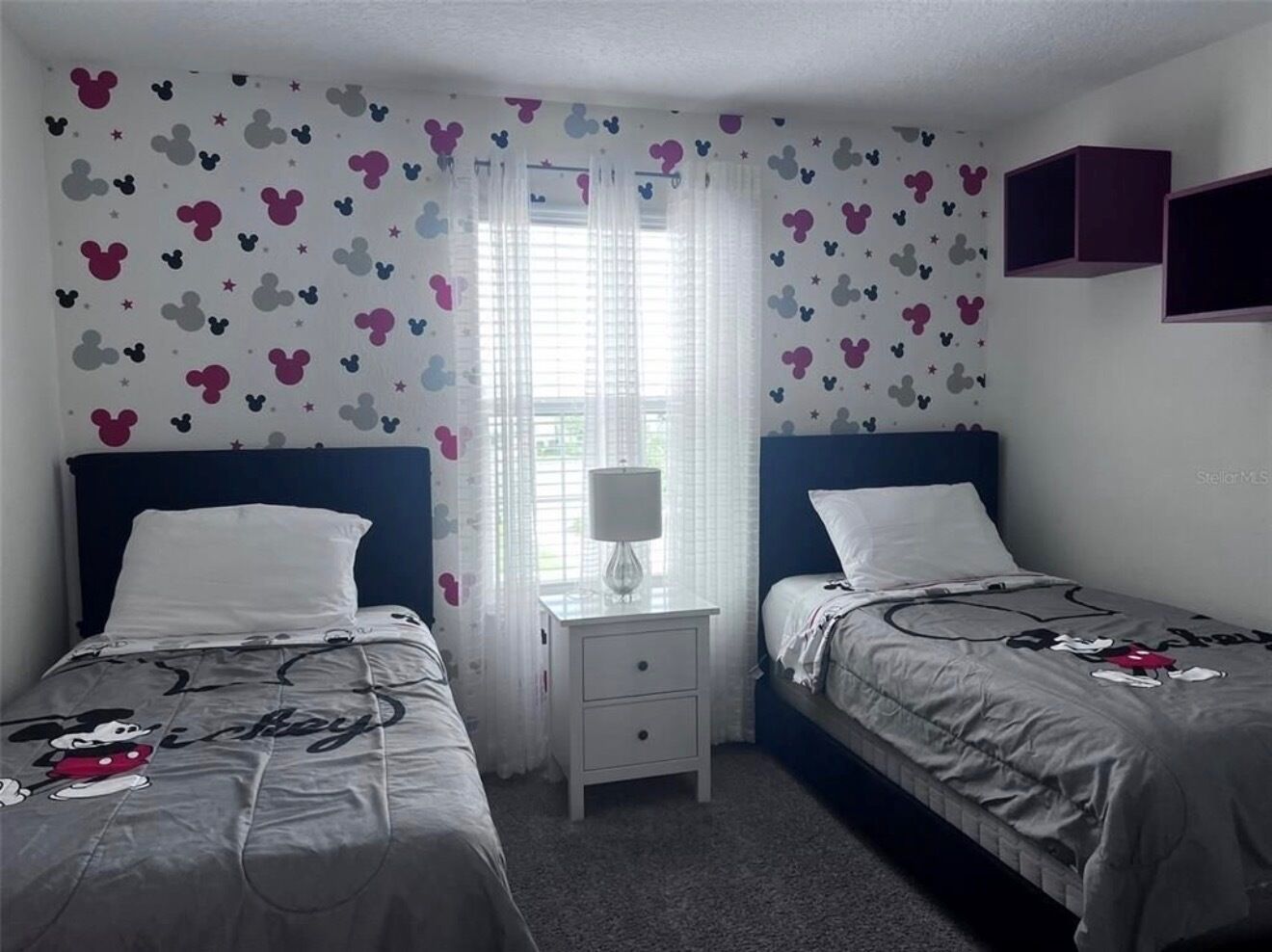 A twin bedroom with two beds, a nightstand, and a window with curtains.