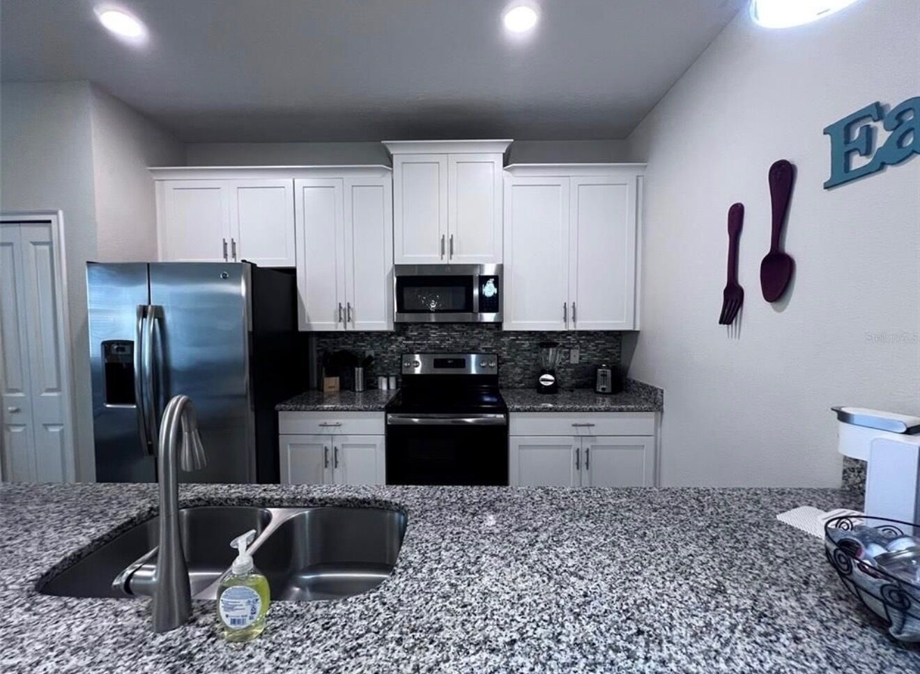 A kitchen with white cabinets, stainless steel appliances, granite countertops, and a built-in microwave.