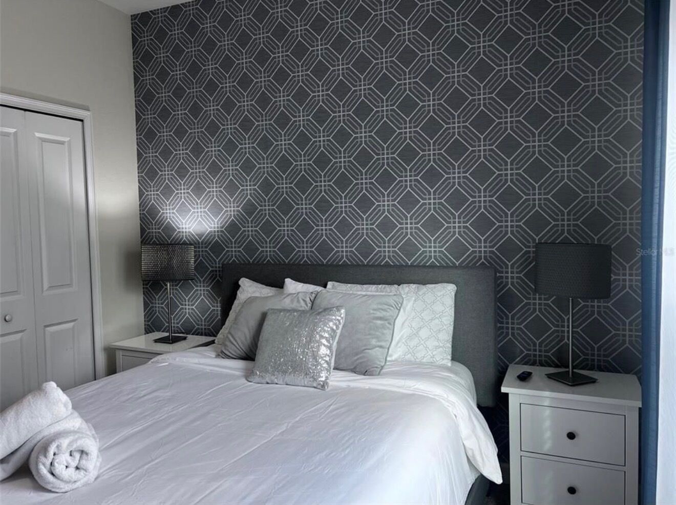 A hotel room with a bed, two bedside tables, a lamp, and a patterned wall.