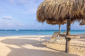 A beach with thatched umbrellas, lounge chairs, and a clear view of the sea with boats. - Aruba Marriott Surf Club - Oceanside 1 bedroom Studio with kitchenette, sleeps 4 (Noord)