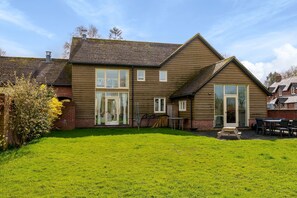 A two-story house with a large front lawn, a patio with outdoor furniture, and a garage. - Byre House (Sleeps 6) - Sutton Waldron , Shaftesbury sleeps 6 guests  in 3 bedrooms (Blandford)
