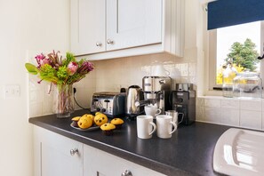 A kitchen with white cabinets, a coffee machine, a toaster, a vase with flowers, and a plate of muffins. - Byre House (Sleeps 6) - Sutton Waldron , Shaftesbury sleeps 6 guests  in 3 bedrooms (Blandford)