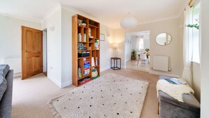 A living room with a bookshelf, a grey sofa, a small table, and a window with curtains. - Byre House (Sleeps 4) - Sutton Waldron , Shaftesbury sleeps 4 guests  in 2 bedrooms (Blandford)