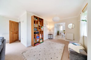 A living room with a bookshelf, a grey sofa, a small table, and a window with curtains. - Byre House (Sleeps 4) - Sutton Waldron , Shaftesbury sleeps 4 guests  in 2 bedrooms (Blandford)