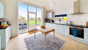 A modern kitchen with a large sliding glass door leading to a patio, a dining area with outdoor furniture, and a view of the garden. - Byre House (Sleeps 4) - Sutton Waldron , Shaftesbury sleeps 4 guests  in 2 bedrooms (Blandford)