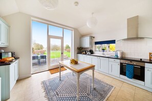 A modern kitchen with a large sliding glass door leading to a patio, a dining area with outdoor furniture, and a view of the garden. - Byre House (Sleeps 4) - Sutton Waldron , Shaftesbury sleeps 4 guests  in 2 bedrooms (Blandford)