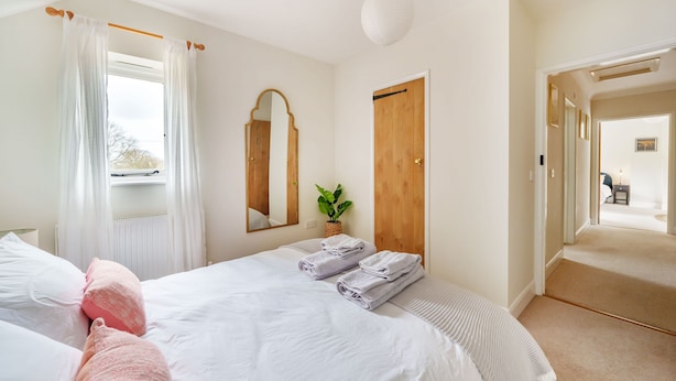 A bedroom with a bed, a window with curtains, a mirror, a wooden door, and a plant. - Byre House (Sleeps 4) - Sutton Waldron , Shaftesbury sleeps 4 guests  in 2 bedrooms (Blandford)