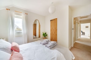Ein Schlafzimmer mit einem Bett, einem Spiegel, einer Holztür und Blick auf den Flur.