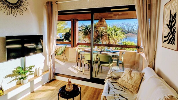 Una sala de estar moderna con un sofá, un televisor, una lámpara colgante y vistas al exterior.