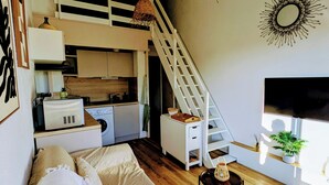 Un dormitorio estilo loft con escaleras, kitchenette y un ventanal grande.