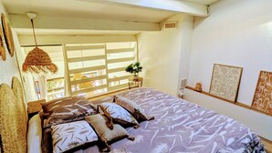 Un dormitorio con cama, almohadas, lámpara colgante, ventana y tragaluz.