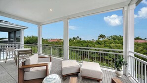 A covered outdoor area with a table and chairs, a cushioned seating area, and a view of greenery and a body of water. - Luxury Waterfront Home with Private Dock and Pool Manatee Cove at Hunters Point (Cortez)