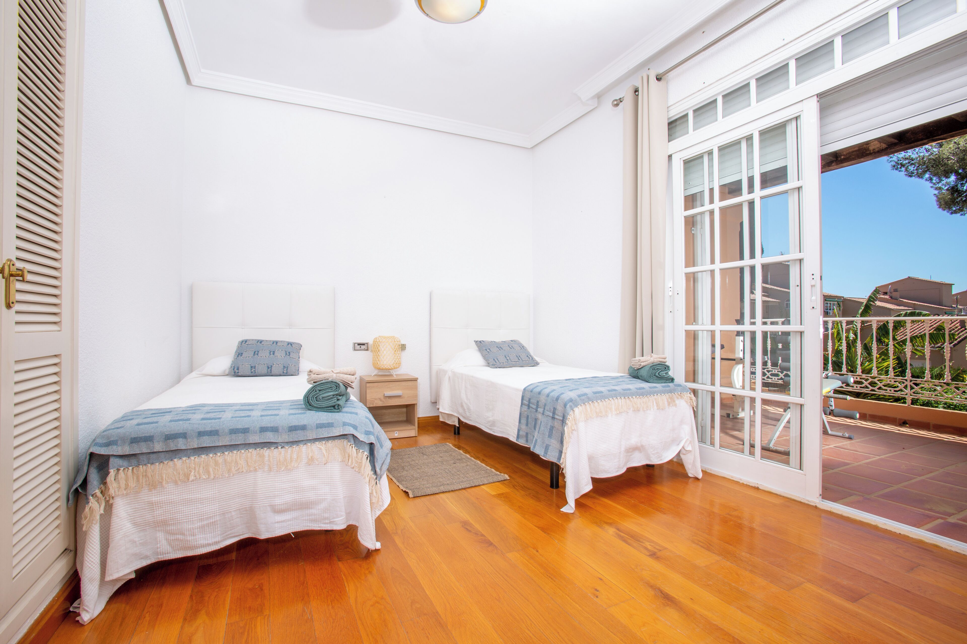 A bedroom with two beds, a wooden floor, a window, and a door leading to an outdoor area.