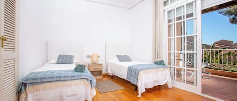 A bedroom with two beds, a wooden floor, a window, and a door leading to an outdoor area.