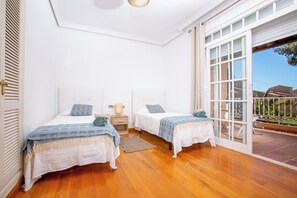 A bedroom with two beds, a wooden floor, a window, and a door leading to an outdoor area. - LXR Villa Elysée: 4 Bedrooms, Pool, and Amenities (AN)