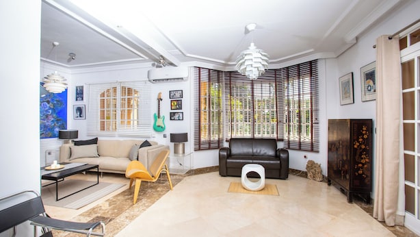 A spacious living room with a sofa, a coffee table, a lamp, and a guitar. - LXR Villa Elysée: 4 Bedrooms, Pool, and Amenities (AN)