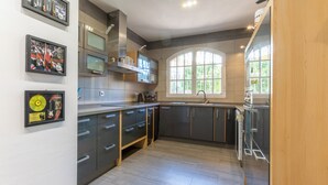 A modern kitchen with grey cabinets, a stainless steel range hood, and a window with a view of greenery. - LXR Villa Elysée: 4 Bedrooms, Pool, and Amenities (AN)