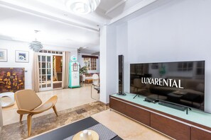 Ein modernes Wohnzimmer mit Flachbildfernseher, einer Couch, einem Couchtisch und einem Essbereich im Hintergrund.