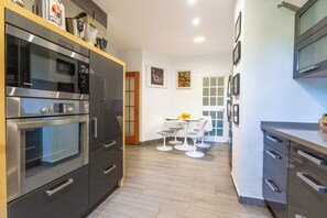 A modern kitchen with stainless steel appliances, a dining area with a white table and chairs, and framed pictures on the wall. - LXR Villa Elysée: 4 Bedrooms, Pool, and Amenities (AN)