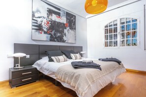 A modern bedroom with a large bed, bedside tables, a nightstand, a wall-mounted abstract painting, a window with a view, and a hanging light fixture. - LXR Villa Elysée: 4 Bedrooms, Pool, and Amenities (AN)