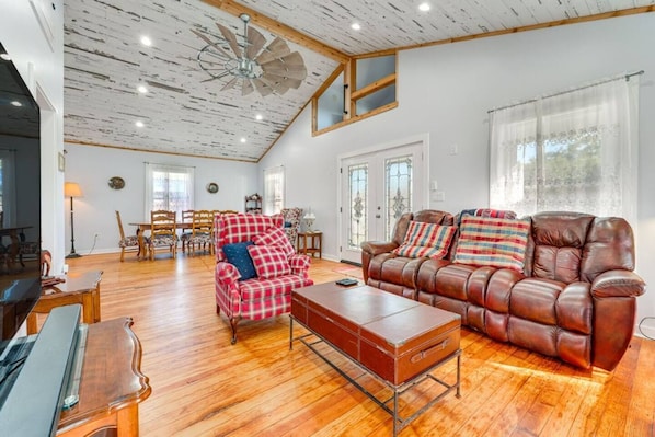 A spacious living room with a brown leather sofa, plaid armchair, and a wooden coffee table.