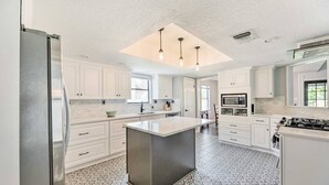 Una cucina moderna con mobili bianchi, un'isola centrale, un frigorifero in acciaio inossidabile e un piano cottura a gas.