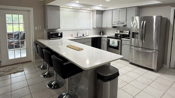 Een moderne keuken met een centraal eiland, roestvrijstalen apparatuur en uitzicht op buiten.