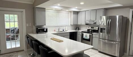 A modern kitchen with a central island, stainless steel appliances, and a view to the outside.