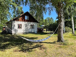 A wooden cabin with a brick exterior, a hammock, and a tree in the foreground. - 6 Person Holiday Home in Byxelkrok (Byxelkrok)